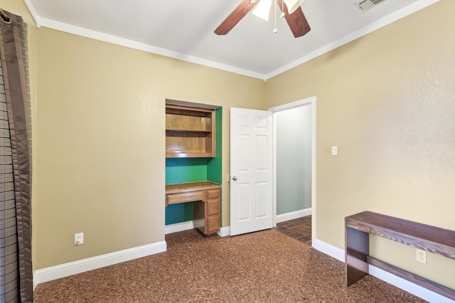 unfurnished bedroom featuring ceiling fan, ornamental molding, built in desk, and dark colored carpet