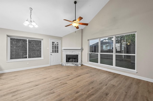 unfurnished living room featuring ceiling fan with notable chandelier, a stone fireplace, high vaulted ceiling, and light hardwood / wood-style flooring