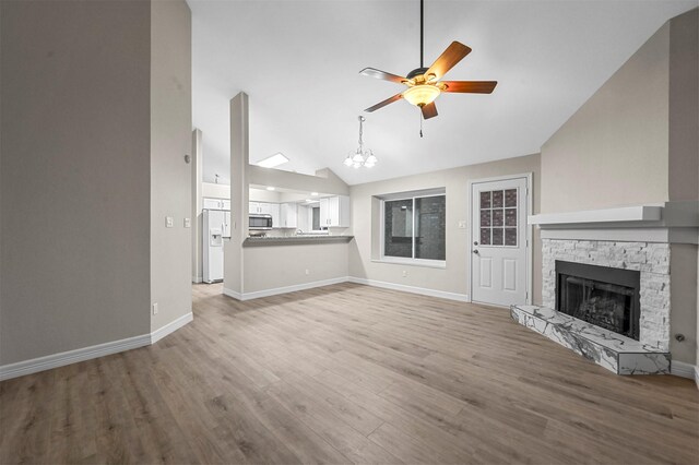 unfurnished living room with ceiling fan with notable chandelier, light wood-type flooring, a stone fireplace, and lofted ceiling