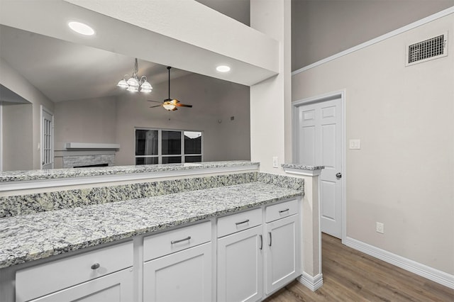 kitchen featuring ceiling fan with notable chandelier, vaulted ceiling, light hardwood / wood-style flooring, light stone counters, and white cabinetry