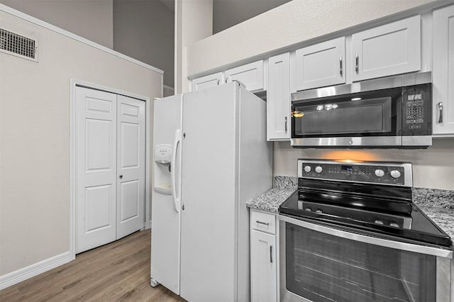 kitchen with light stone counters, white cabinets, stainless steel appliances, and light wood-type flooring