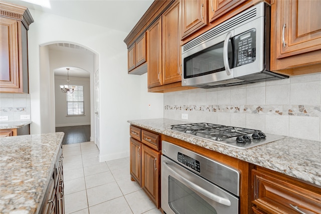 kitchen with tasteful backsplash, light stone counters, an inviting chandelier, and appliances with stainless steel finishes