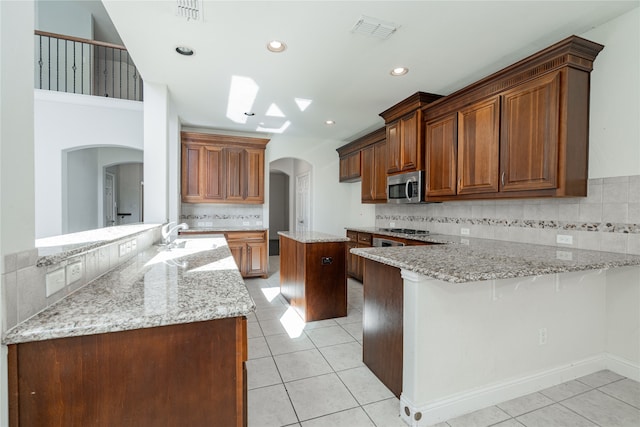 kitchen featuring kitchen peninsula, backsplash, stainless steel appliances, and light stone countertops