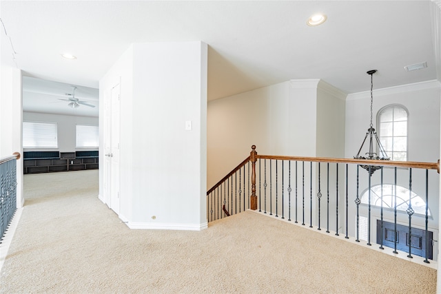 corridor featuring a healthy amount of sunlight, crown molding, light colored carpet, and an inviting chandelier