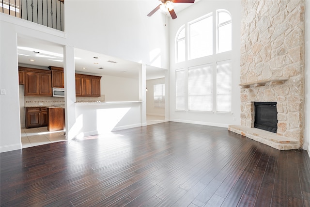 unfurnished living room featuring ceiling fan, light hardwood / wood-style floors, a fireplace, and a high ceiling