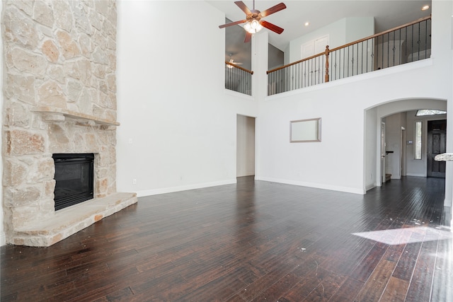 unfurnished living room featuring a towering ceiling, dark hardwood / wood-style floors, a stone fireplace, and ceiling fan