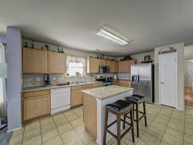 kitchen with backsplash, a kitchen breakfast bar, sink, a kitchen island, and stainless steel appliances