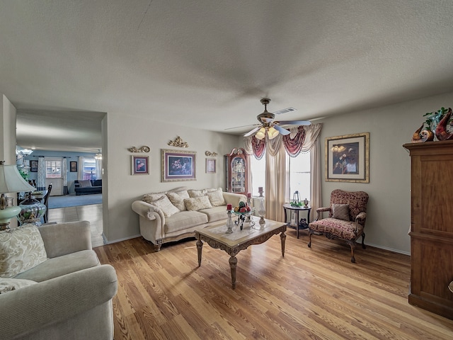 living room with ceiling fan, light hardwood / wood-style flooring, a healthy amount of sunlight, and a textured ceiling