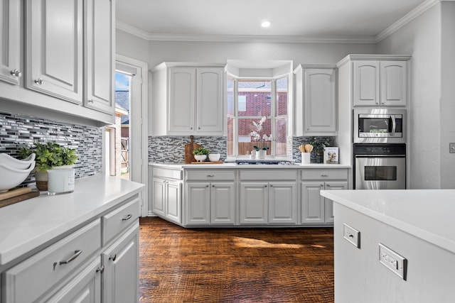 kitchen with dark hardwood / wood-style flooring, backsplash, stainless steel appliances, crown molding, and white cabinetry