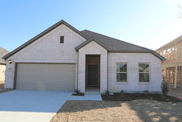 view of front of home with driveway, an attached garage, roof with shingles, and brick siding