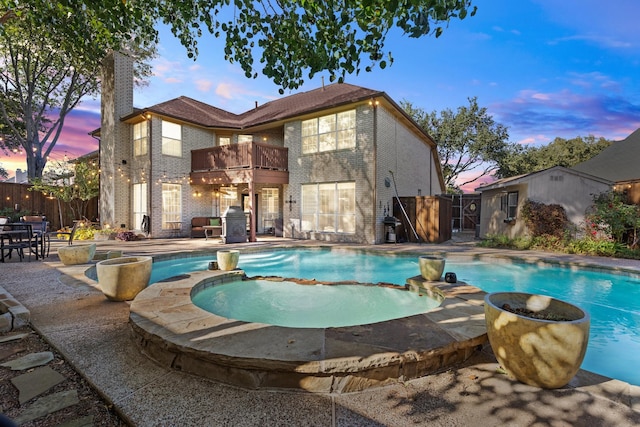 pool at dusk with fence and a pool with connected hot tub