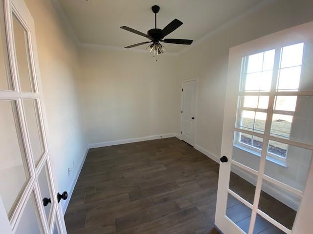 empty room with crown molding, ceiling fan, and dark wood-type flooring