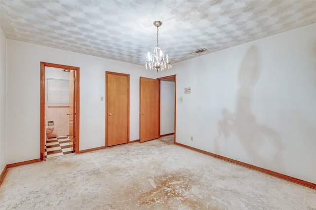 unfurnished bedroom featuring multiple closets, ensuite bathroom, a textured ceiling, and an inviting chandelier