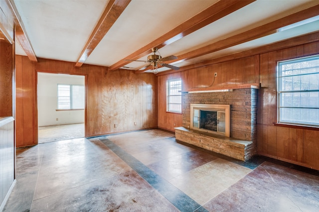 unfurnished living room with beam ceiling, a stone fireplace, wooden walls, and ceiling fan