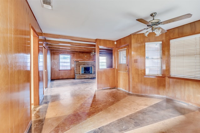 interior space featuring ceiling fan, concrete flooring, a fireplace, and wooden walls