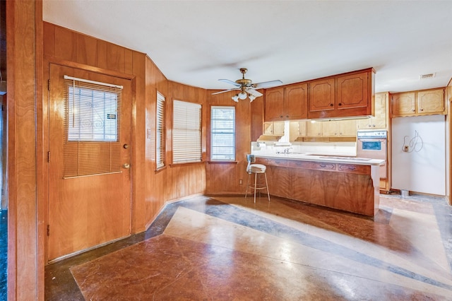 kitchen featuring kitchen peninsula, ceiling fan, wood walls, and stainless steel oven