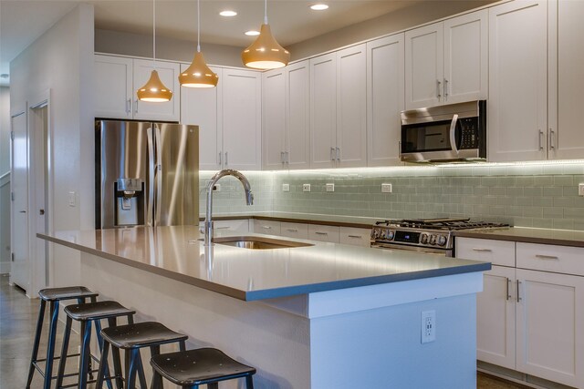 kitchen with sink, an island with sink, appliances with stainless steel finishes, decorative light fixtures, and white cabinetry