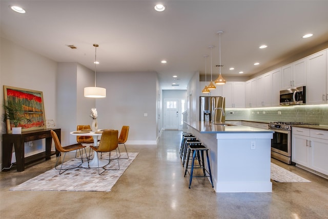 kitchen with white cabinets, decorative light fixtures, stainless steel appliances, and an island with sink