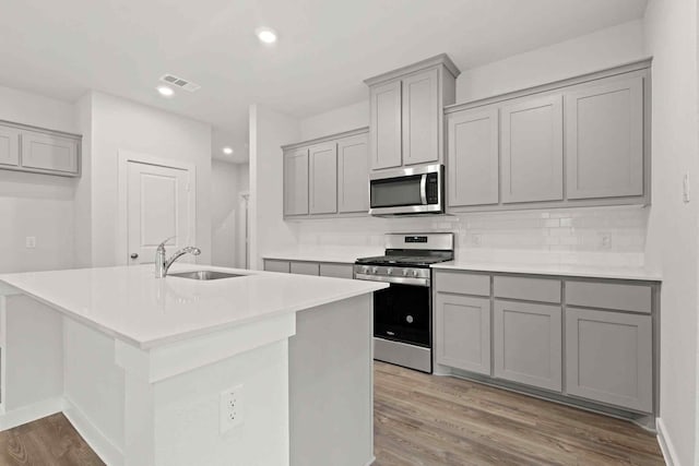 kitchen with stainless steel appliances, an island with sink, sink, and gray cabinets