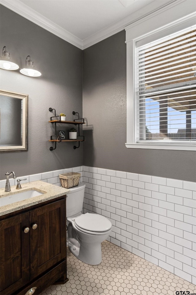 bathroom with tile patterned flooring, crown molding, toilet, vanity, and tile walls