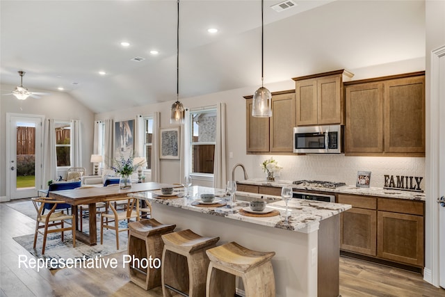 kitchen with light hardwood / wood-style flooring, an island with sink, stainless steel appliances, and vaulted ceiling