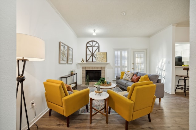 living room with a tiled fireplace, wood-type flooring, a textured ceiling, and ornamental molding