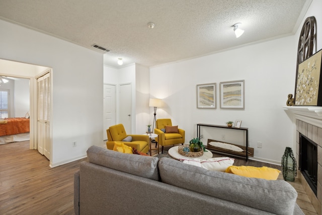 living room featuring hardwood / wood-style flooring, ceiling fan, ornamental molding, a fireplace, and a textured ceiling