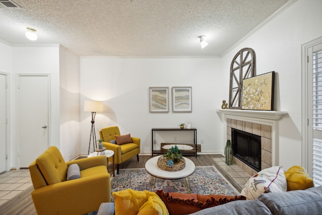 living room featuring a tile fireplace, a textured ceiling, light wood-type flooring, and crown molding