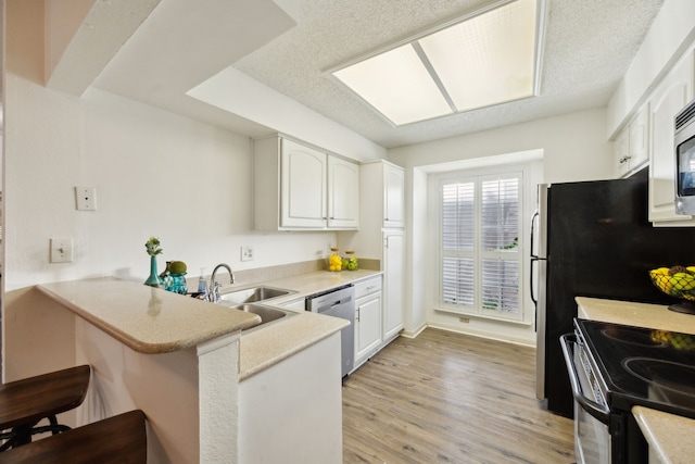 kitchen with kitchen peninsula, appliances with stainless steel finishes, a breakfast bar, light hardwood / wood-style flooring, and white cabinetry