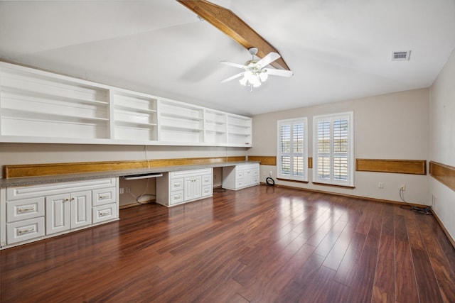 unfurnished office with ceiling fan, lofted ceiling with beams, dark hardwood / wood-style flooring, and built in desk