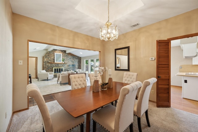 dining room featuring a fireplace, a chandelier, lofted ceiling, and light wood-type flooring