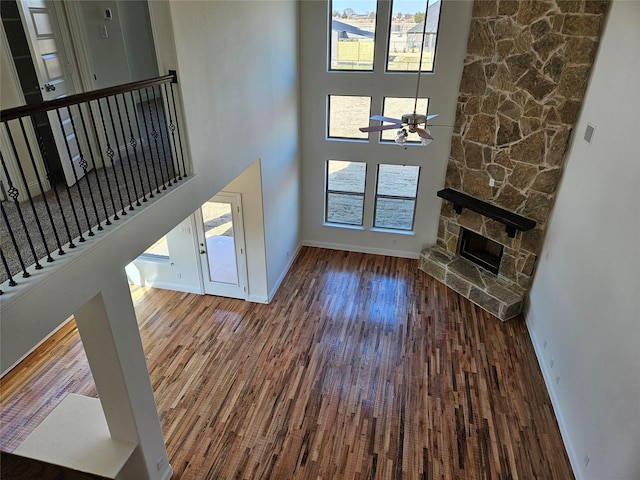 unfurnished living room featuring a high ceiling, wood-type flooring, ceiling fan, and a fireplace