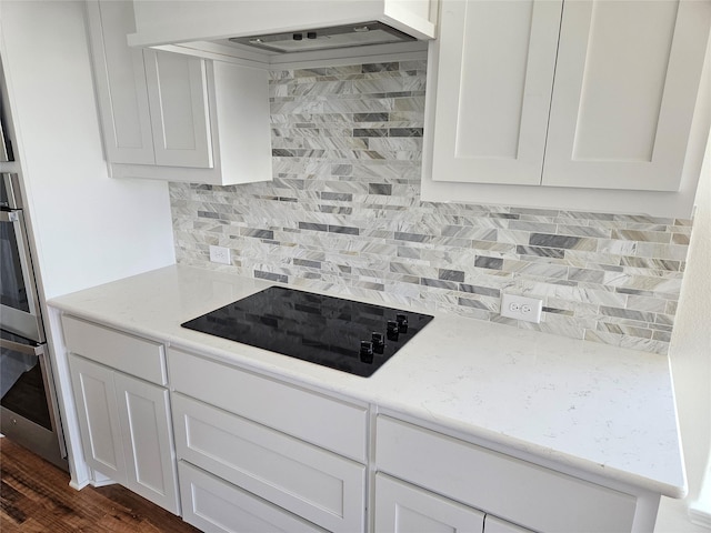 kitchen with black electric cooktop, backsplash, white cabinets, and premium range hood