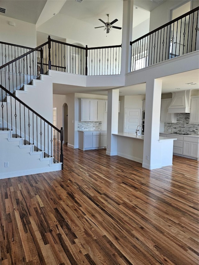 unfurnished living room with a high ceiling, dark hardwood / wood-style flooring, sink, and ceiling fan