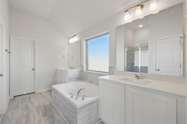 bathroom with a garden tub, two vanities, vaulted ceiling, a sink, and a shower stall