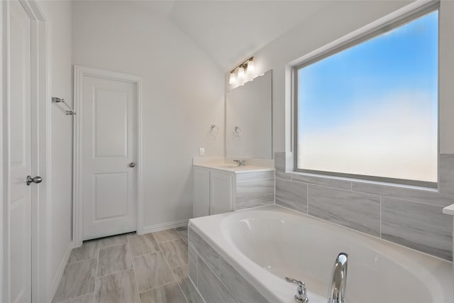 bathroom featuring a garden tub, vaulted ceiling, vanity, and baseboards