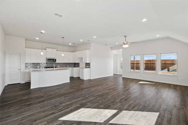 kitchen featuring stainless steel microwave, visible vents, backsplash, open floor plan, and an island with sink