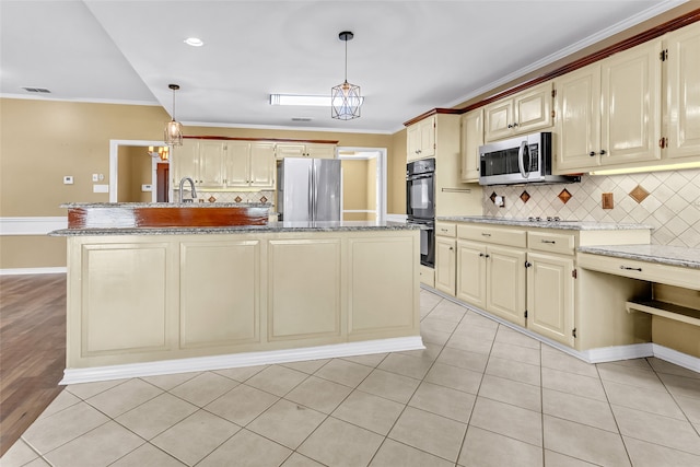 kitchen featuring decorative light fixtures, stainless steel appliances, a center island with sink, and cream cabinets