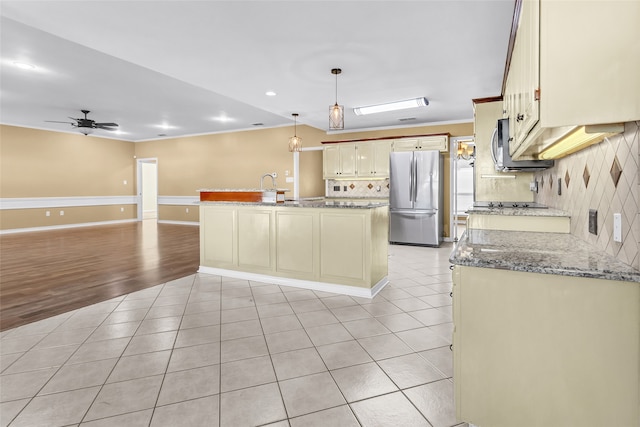 kitchen with appliances with stainless steel finishes, light wood-type flooring, backsplash, a center island with sink, and hanging light fixtures