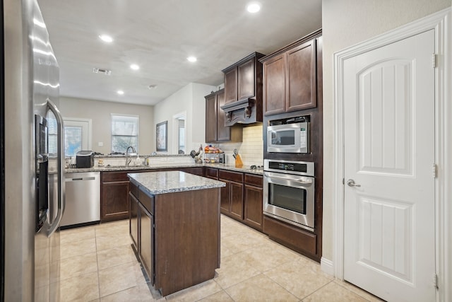 kitchen featuring light stone countertops, a center island, sink, light tile patterned flooring, and appliances with stainless steel finishes