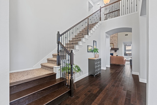 stairs with visible vents, baseboards, arched walkways, wood finished floors, and a high ceiling