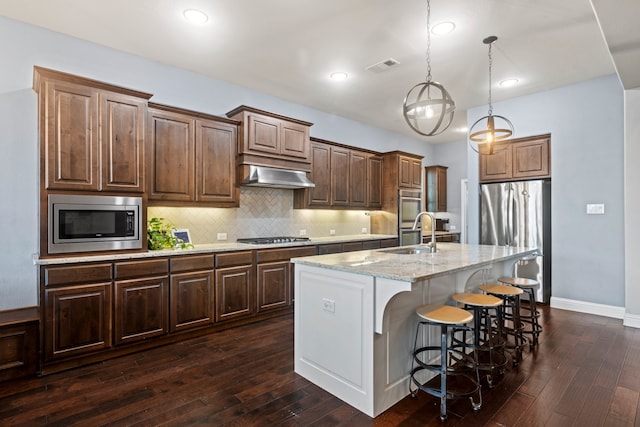 kitchen featuring sink, appliances with stainless steel finishes, hanging light fixtures, extractor fan, and a center island with sink