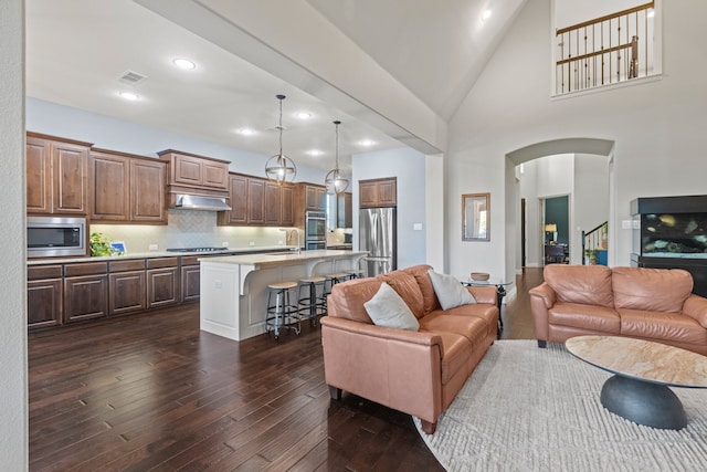 living area with visible vents, arched walkways, dark wood-style floors, high vaulted ceiling, and recessed lighting