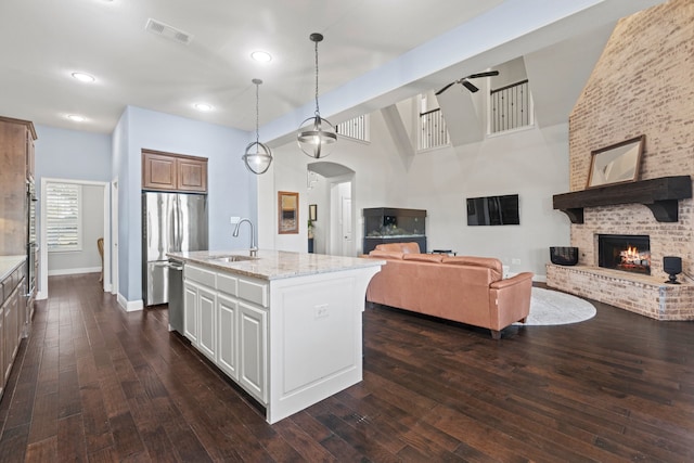 kitchen featuring stainless steel appliances, visible vents, a brick fireplace, open floor plan, and a sink