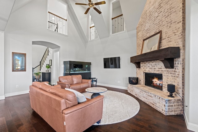 living room with a brick fireplace, baseboards, dark wood-style flooring, and stairs