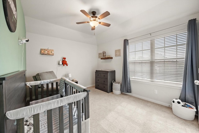 carpeted bedroom with a crib, lofted ceiling, and ceiling fan