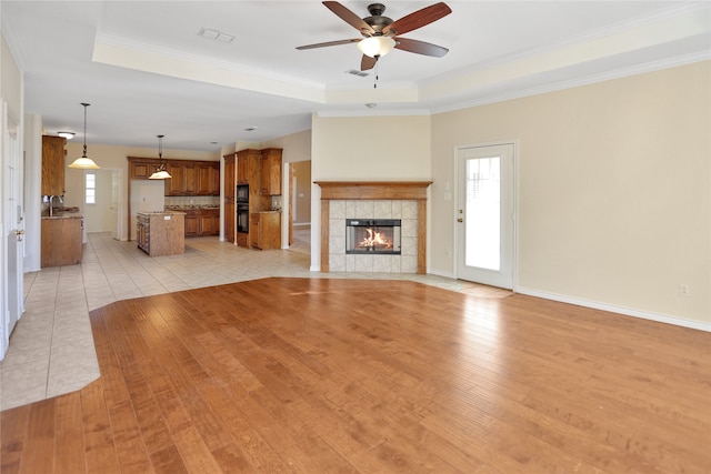 unfurnished living room with a tiled fireplace, crown molding, light wood-type flooring, and a tray ceiling