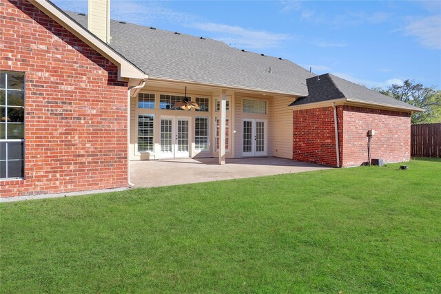 rear view of house featuring a shingled roof, a lawn, french doors, a patio area, and brick siding