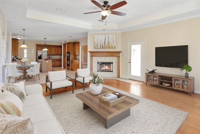 living room with a tile fireplace, a healthy amount of sunlight, light wood-type flooring, and a tray ceiling