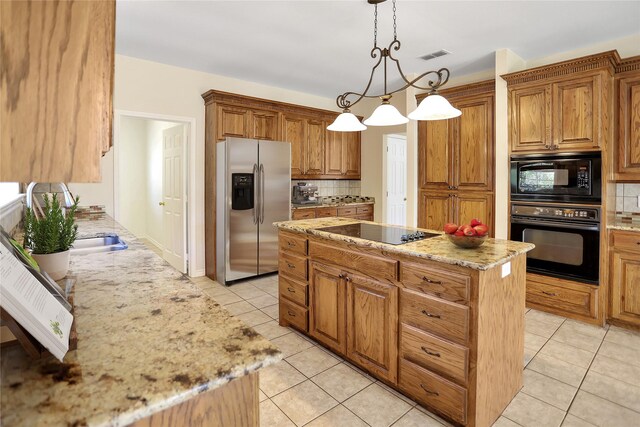 kitchen with visible vents, light stone counters, decorative light fixtures, a center island, and black appliances